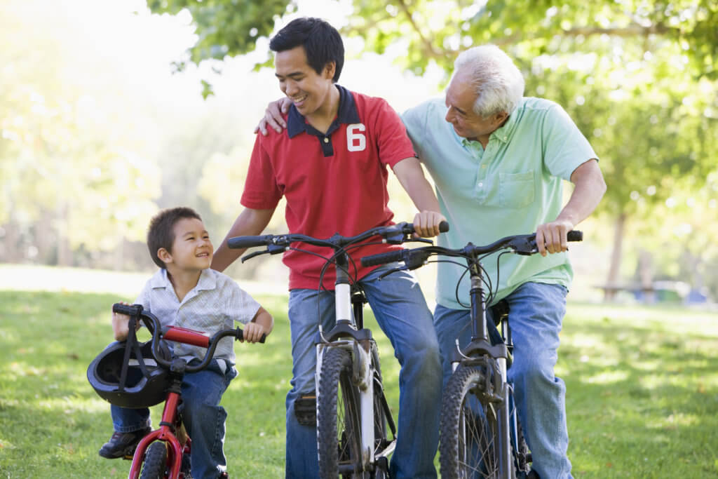 Family of Asian descent -- a little boy, his father and grandfather -- all riding bicycles together.